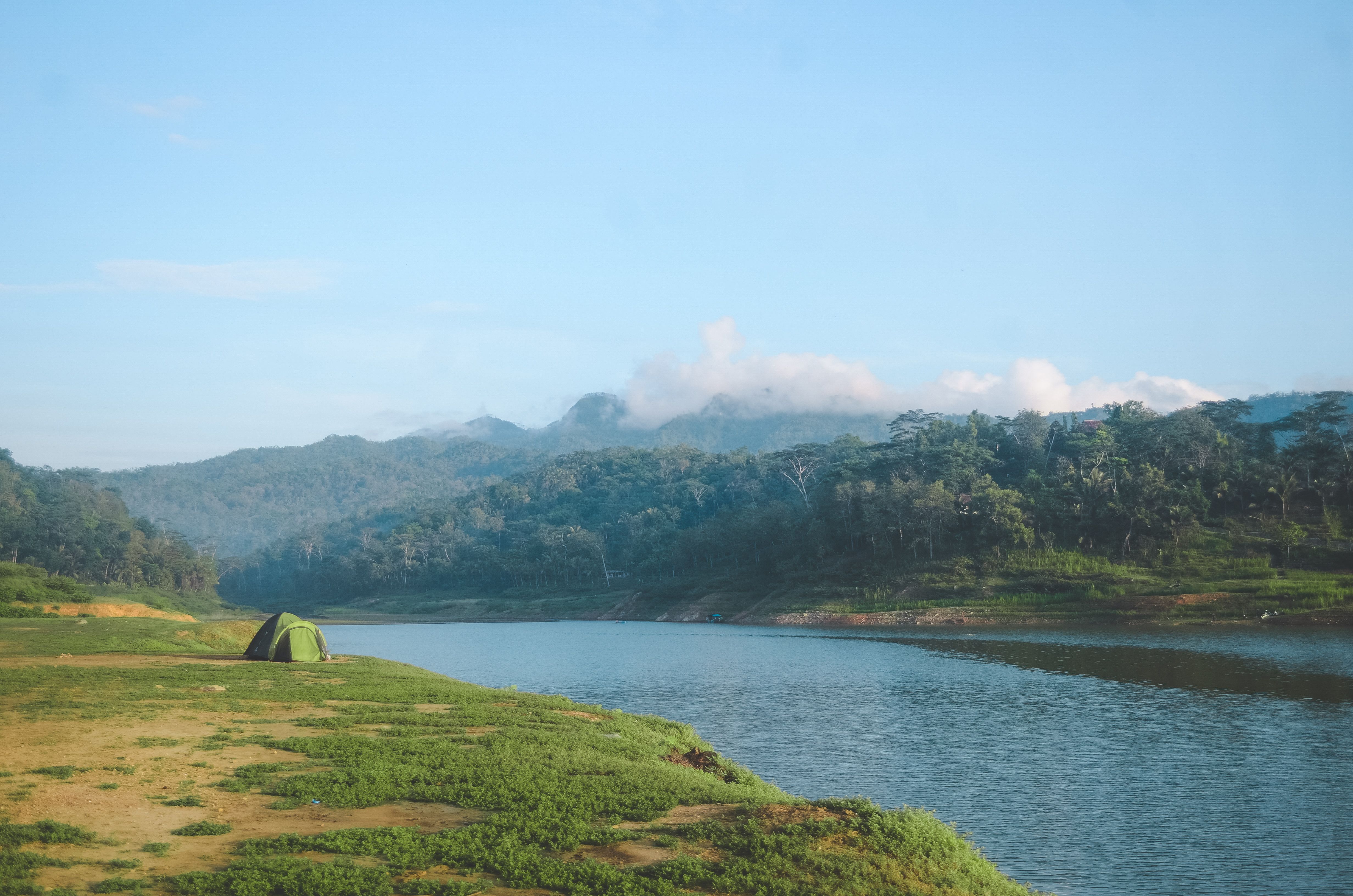 Tent pitched beside an alpine lake surrounded by forested hills and mountains