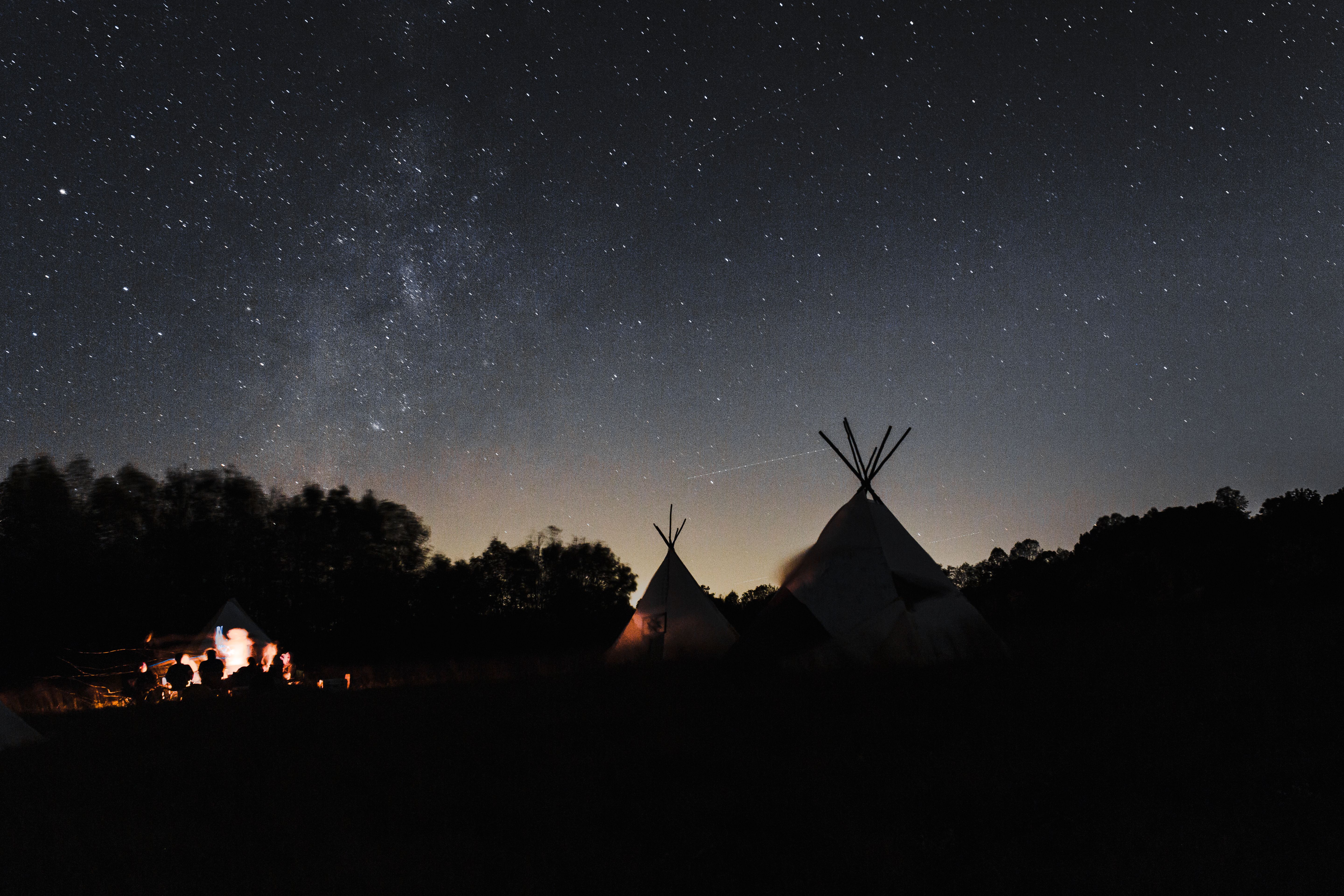 Tende glamping illuminate di notte sotto un cielo stellato, con un falò acceso davanti